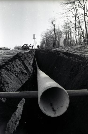 a photo of a water pipe laid in a trench with workmen and a water tower in the background